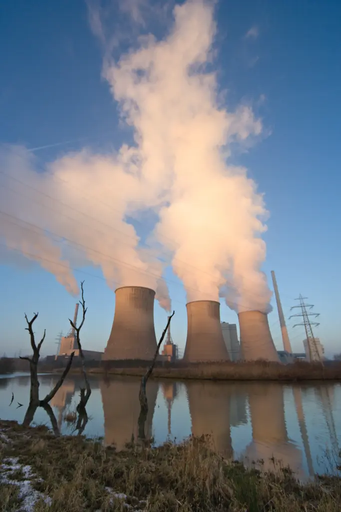 Steam plumes rising from power plant cooling towers reflected in water.