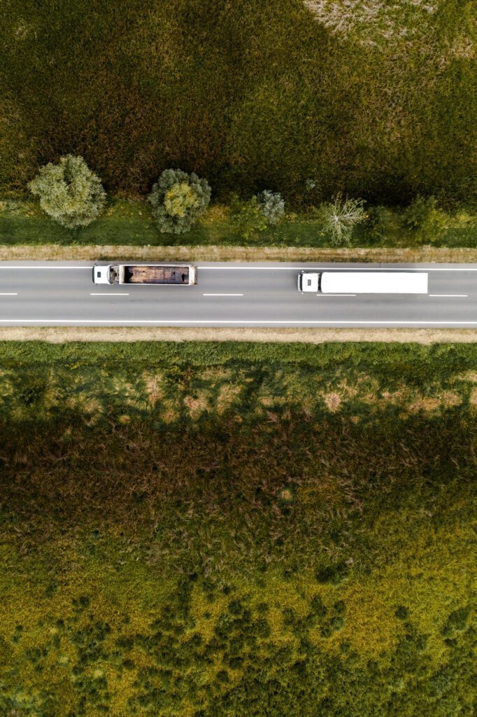 Top-down aerial view of trucks on a road through green fields.
