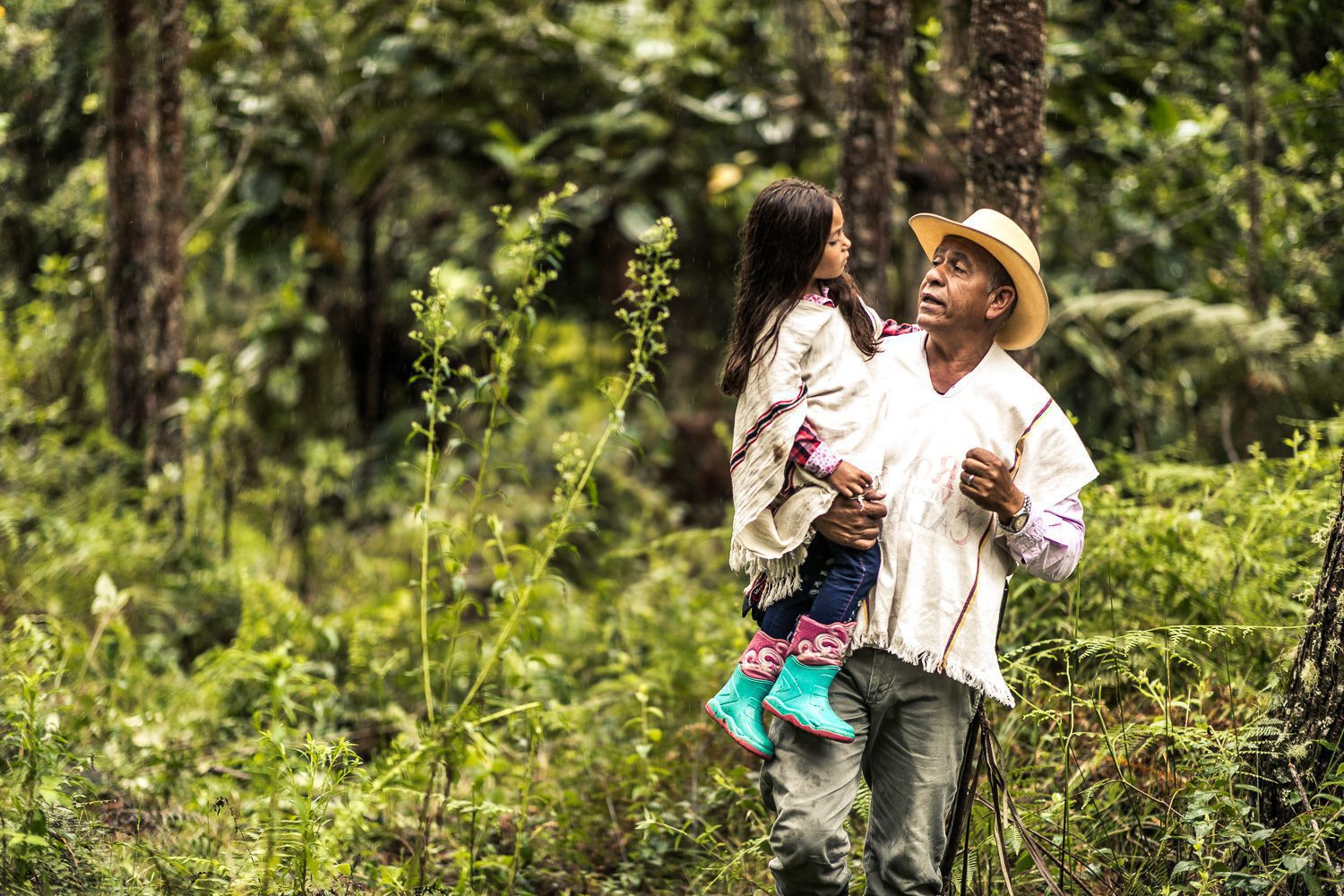 Hombre cargando a una niña en un bosque frondoso.